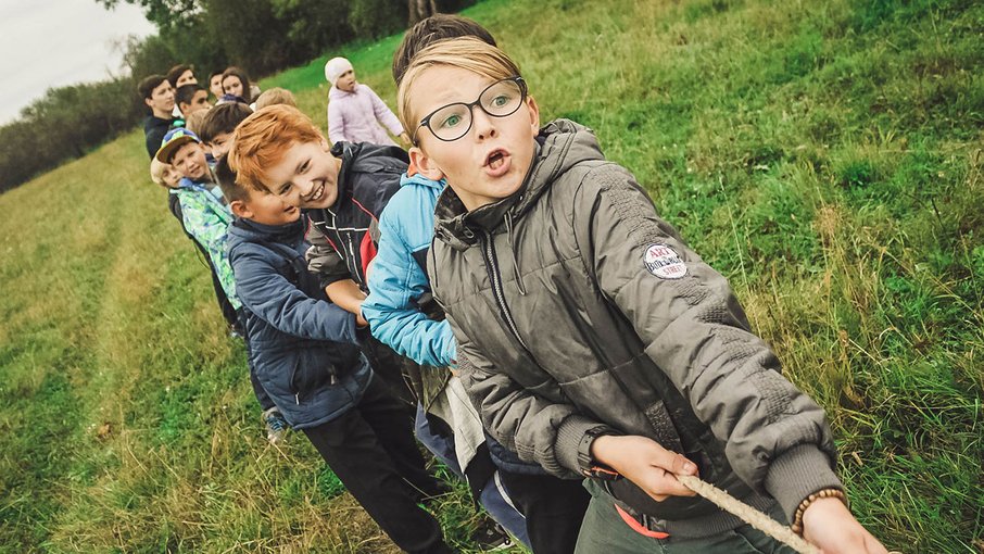 Kinder stehen in einer Reihe hintereinander und ziehen ein Tau 