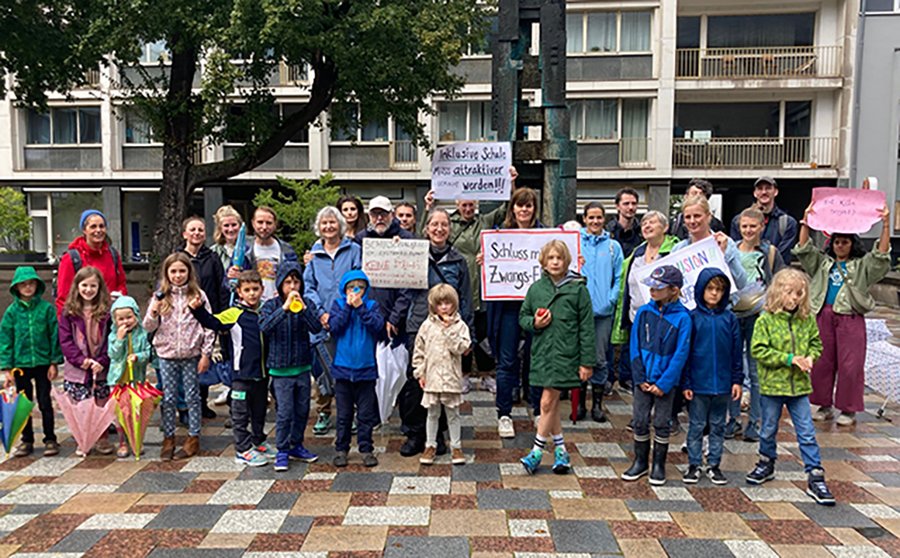 Etwa 30 Erwachsende und Kinder stehen zusammen und halten Schilder in die Höhe