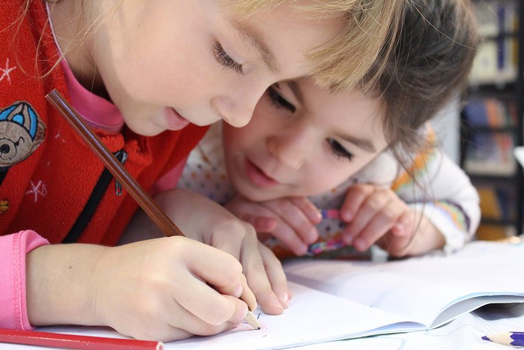 Nahaufnahme zweier Kinder, die über ein Heft gebeugt sind. Eines von ihnen schreibt etwas in das Heft.