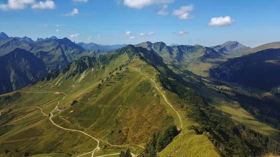 Eine grüne Berglandschaft, oben im Bild blauer Himmel mit einigen weißen Wolken.