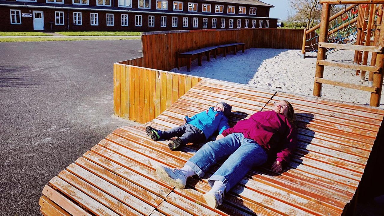 Ninia und Sohn liegend auf einer Bank, die Sonne scheint ihnen ins Gesicht