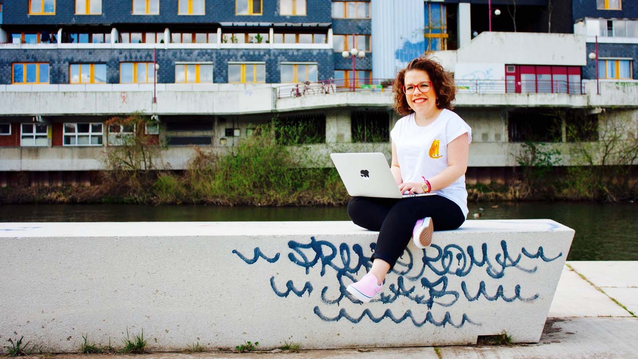 Ninia auf einer mit Grafitti besprühten Mauer sitzend, auf ihrem Schoß ein Laptop 